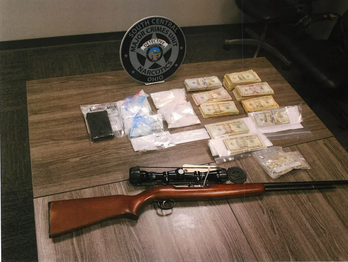 Evidence seized in the Thornville search warrant laid out on a table: bags of suspected drugs, stacks of cash, a scoped rifle and a Major Crimes Unit badge